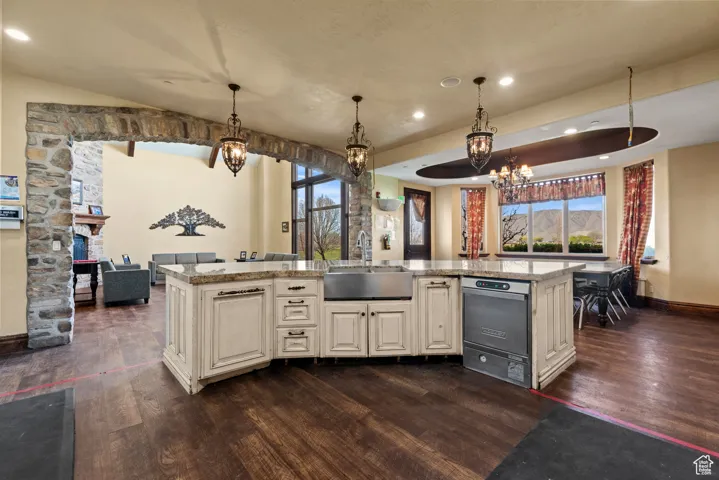 Kitchen featuring light stone countertops, a wealth of natural light, dark wood-style flooring, a sink, and a notable chandelier