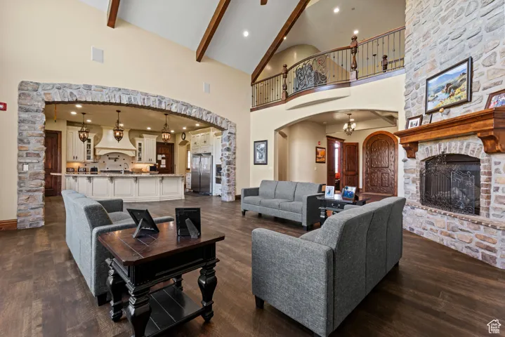 Living area with a stone fireplace, beamed ceiling, dark wood finished floors, high vaulted ceiling, and arched walkways