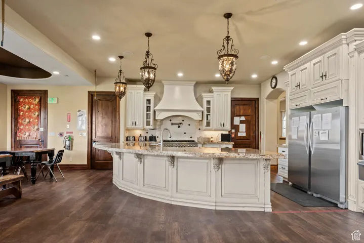 Kitchen featuring custom exhaust hood, baseboards, freestanding refrigerator, and dark wood-type flooring