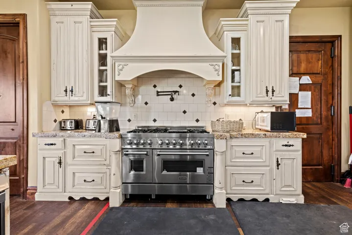 Kitchen featuring custom range hood, white microwave, dark wood-style flooring, and range with two ovens