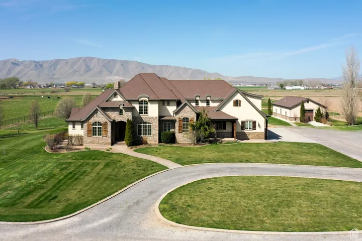 View of front of home featuring curved driveway, stucco siding, stone siding, a front lawn, and a mountain view