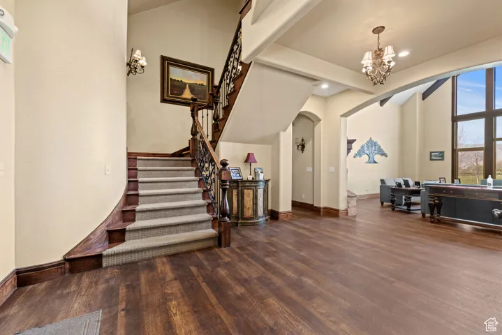 Foyer entrance featuring stairway, arched walkways, a notable chandelier, and wood finished floors