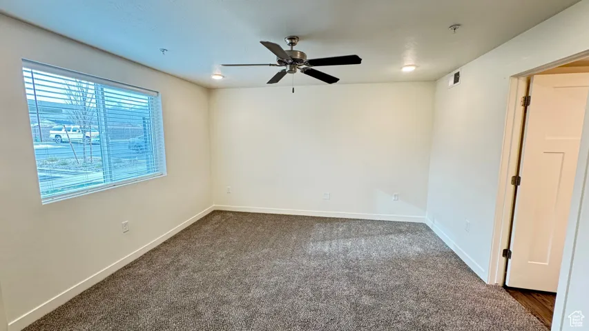 Unfurnished room featuring visible vents, baseboards, dark carpet, and ceiling fan