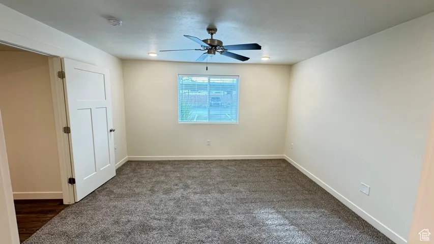 Unfurnished room featuring dark colored carpet, baseboards, and ceiling fan