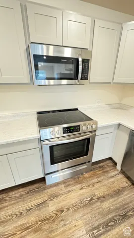 Kitchen with dark wood-type flooring, light countertops, appliances with stainless steel finishes, and white cabinetry