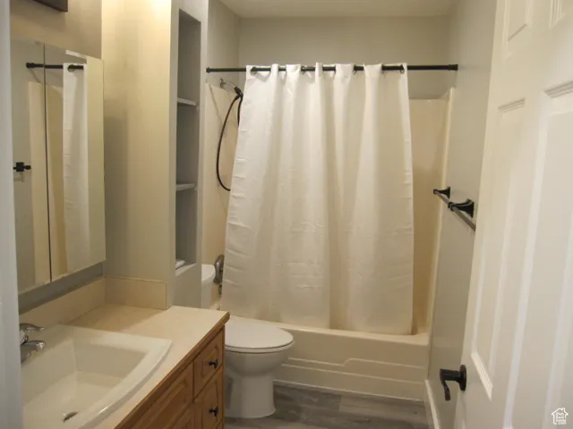 Bathroom with toilet, shower / tub combo, wood finished floors, and vanity
