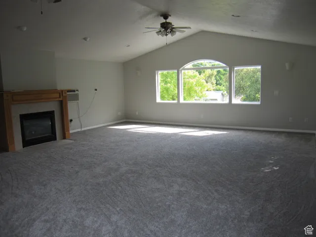 Unfurnished living room featuring baseboards, a tiled fireplace, carpet flooring, a ceiling fan, and lofted ceiling
