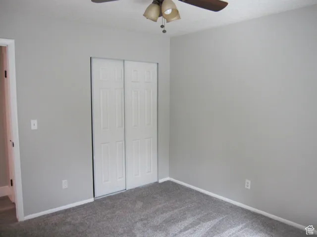 Unfurnished bedroom featuring dark carpet, a closet, baseboards, and a ceiling fan
