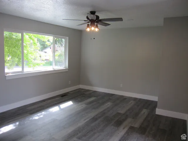 Empty room with dark wood-type flooring, baseboards, a ceiling fan, and a textured ceiling
