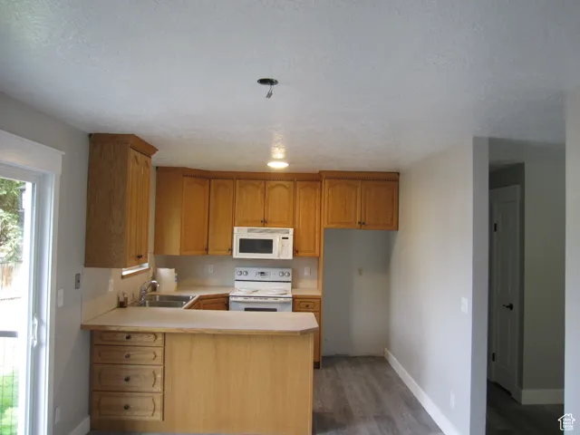 Kitchen with white appliances, light wood-style flooring, a peninsula, light countertops, and a sink