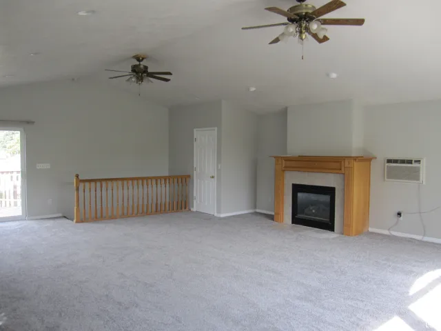 Unfurnished living room with light carpet, ceiling fan, an AC wall unit, and lofted ceiling