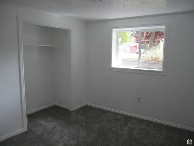 Unfurnished bedroom featuring a closet, baseboards, dark colored carpet, and a textured ceiling