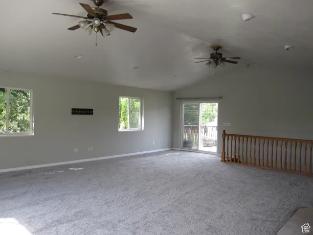 Spare room featuring carpet flooring, baseboards, a ceiling fan, and lofted ceiling