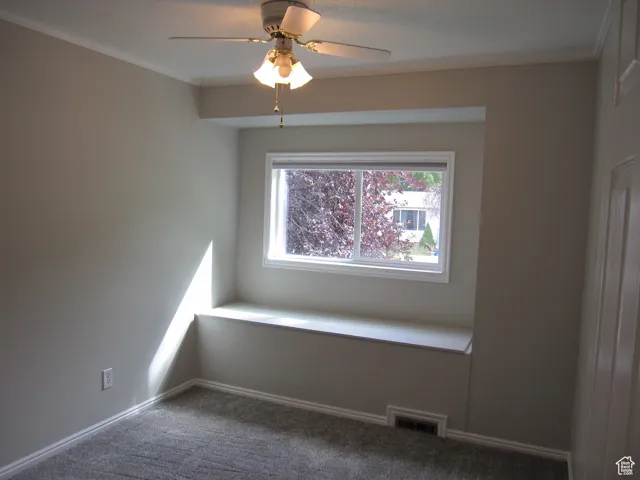 Spare room with carpet, a ceiling fan, ornamental molding, visible vents, and baseboards