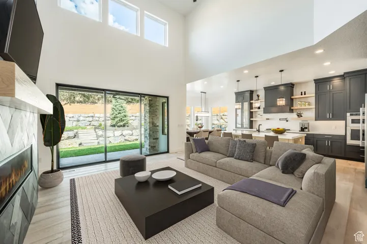 Living room with a towering ceiling, healthy amount of natural light, light wood-style floors, a glass covered fireplace, and recessed lighting