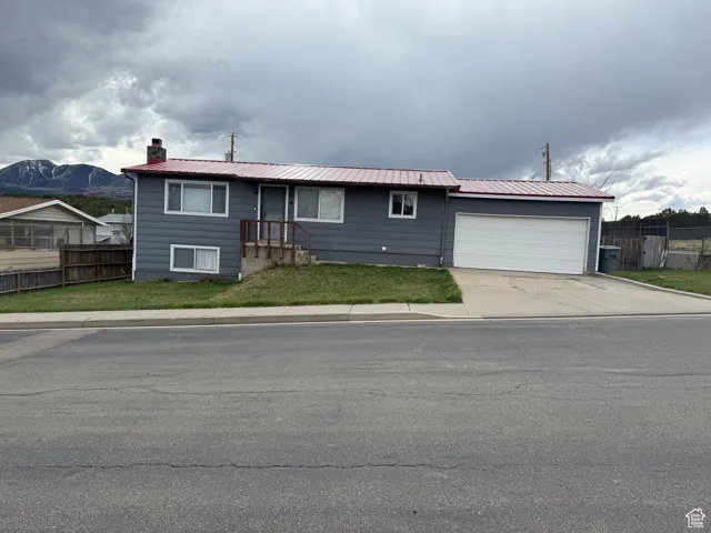 Single story home featuring a chimney, fence, concrete driveway, an attached garage, and a front yard
