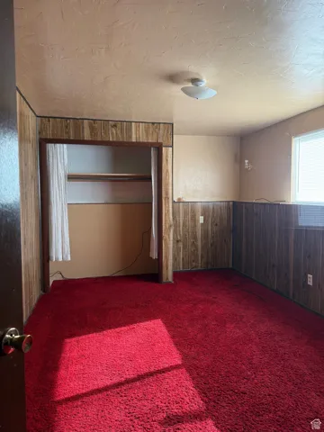 Spare room with a wainscoted wall, wood walls, carpet, and a textured ceiling