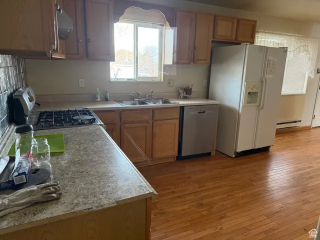 Kitchen with a baseboard heating unit, a sink, white refrigerator with ice dispenser, gas stove, and dishwasher