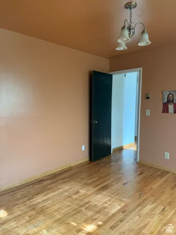 Unfurnished room with an inviting chandelier, light wood finished floors, and baseboards