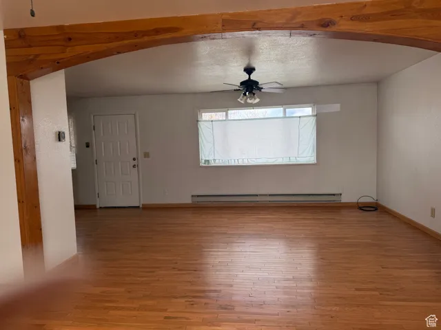 Unfurnished living room featuring arched walkways, light wood-type flooring, baseboards, ceiling fan, and a baseboard radiator