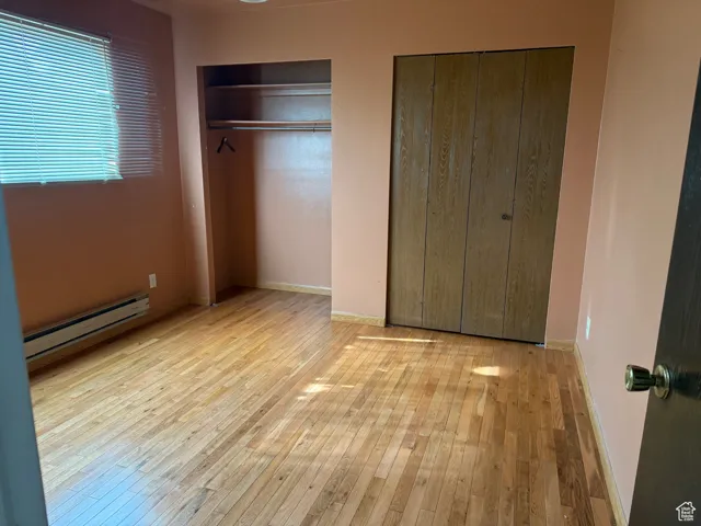 Unfurnished bedroom featuring hardwood / wood-style flooring, a baseboard radiator, baseboards, and two closets