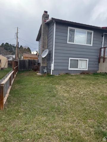 View of side of home with fence, a lawn, and a chimney