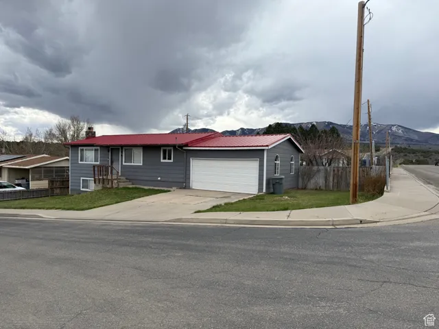 Ranch-style home featuring a chimney, concrete driveway, an attached garage, fence, and a mountain view