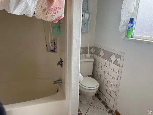 Full bathroom featuring toilet, tile patterned flooring,  shower combination, and tile walls