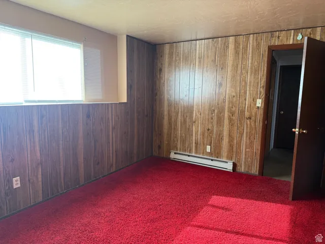 Carpeted spare room with a baseboard radiator and wooden walls