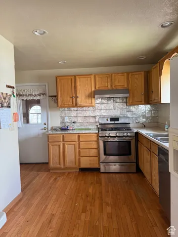 Kitchen featuring dishwasher, under cabinet range hood, stainless steel gas range oven, and light countertops