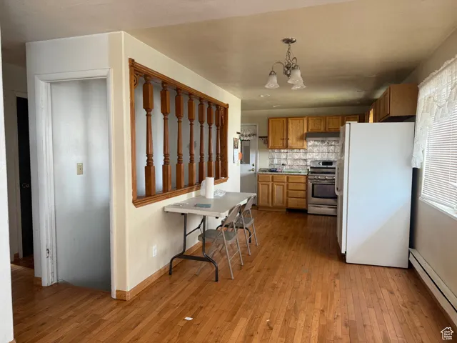Kitchen featuring light wood finished floors, an inviting chandelier, stainless steel range with gas stovetop, freestanding refrigerator, and a baseboard radiator