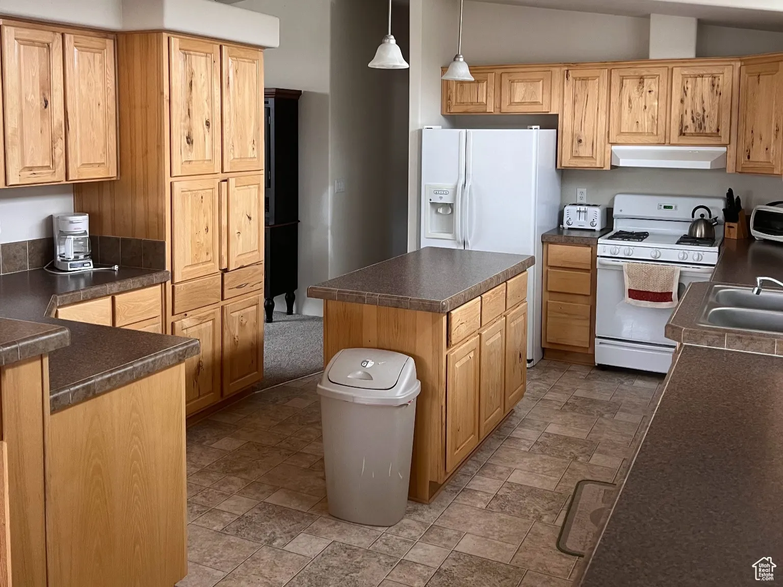 Kitchen featuring under cabinet range hood, stone finish flooring, a kitchen island, white appliances, and dark countertops