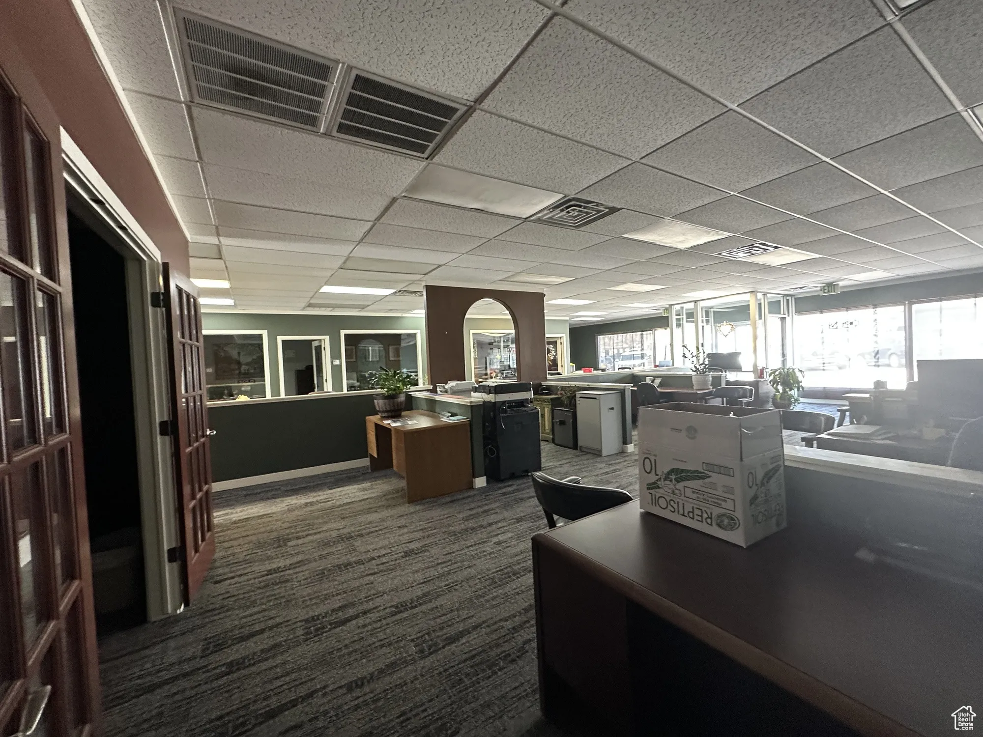 Office with dark colored carpet, visible vents, and a drop ceiling