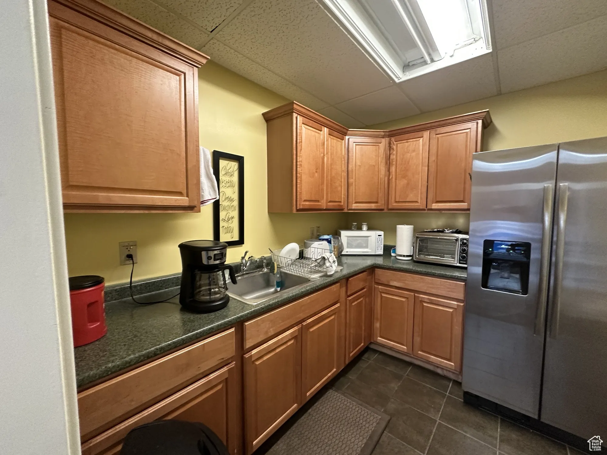 Kitchen with stainless steel refrigerator with ice dispenser, a paneled ceiling, a sink, and dark tile patterned flooring
