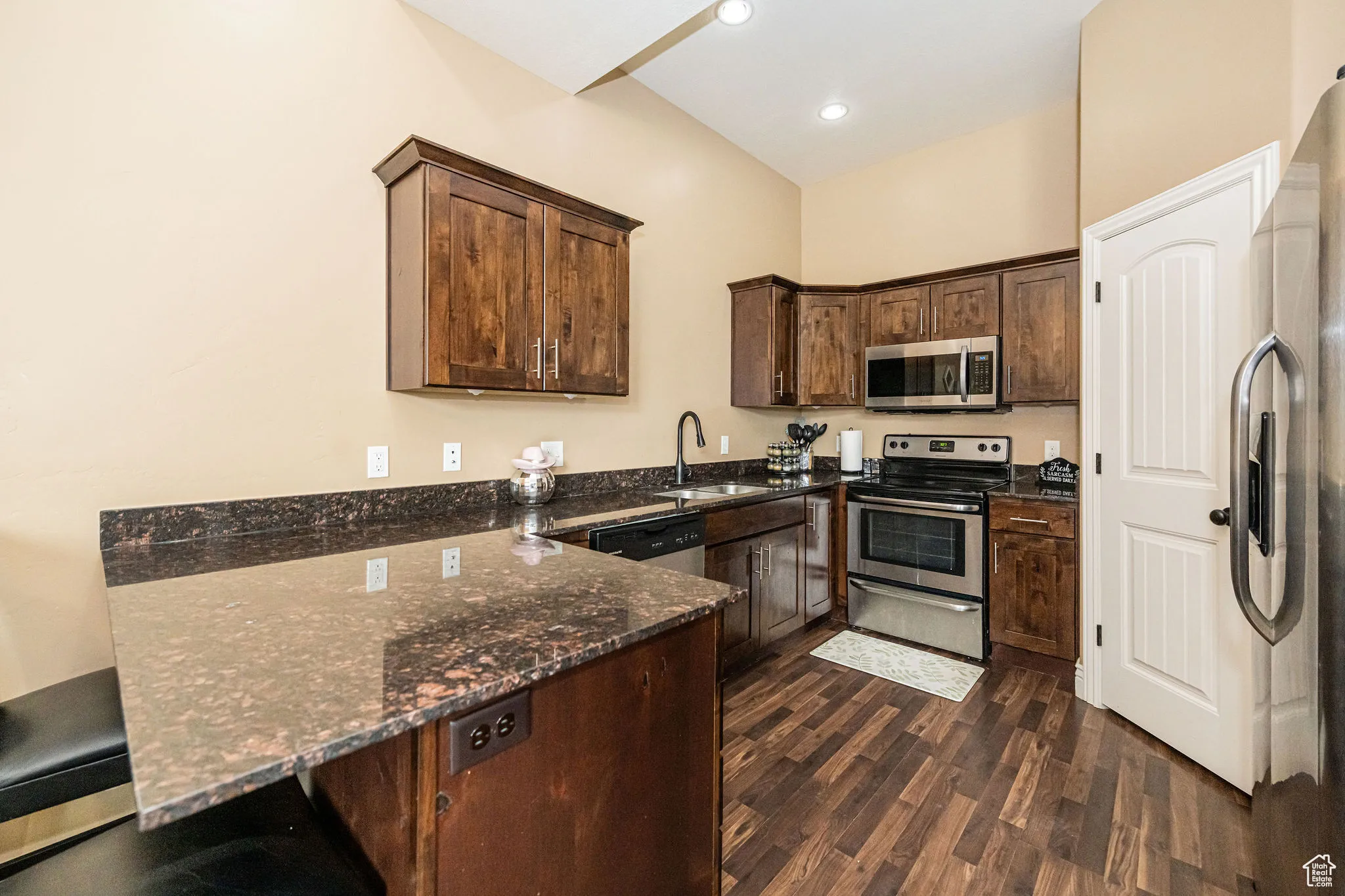 Kitchen with stainless steel appliances, dark stone countertops, a sink, dark wood-type flooring, and dark brown cabinetry