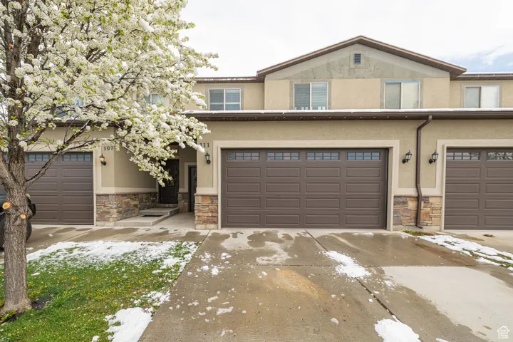 View of front of house featuring driveway, stone siding, and stucco siding