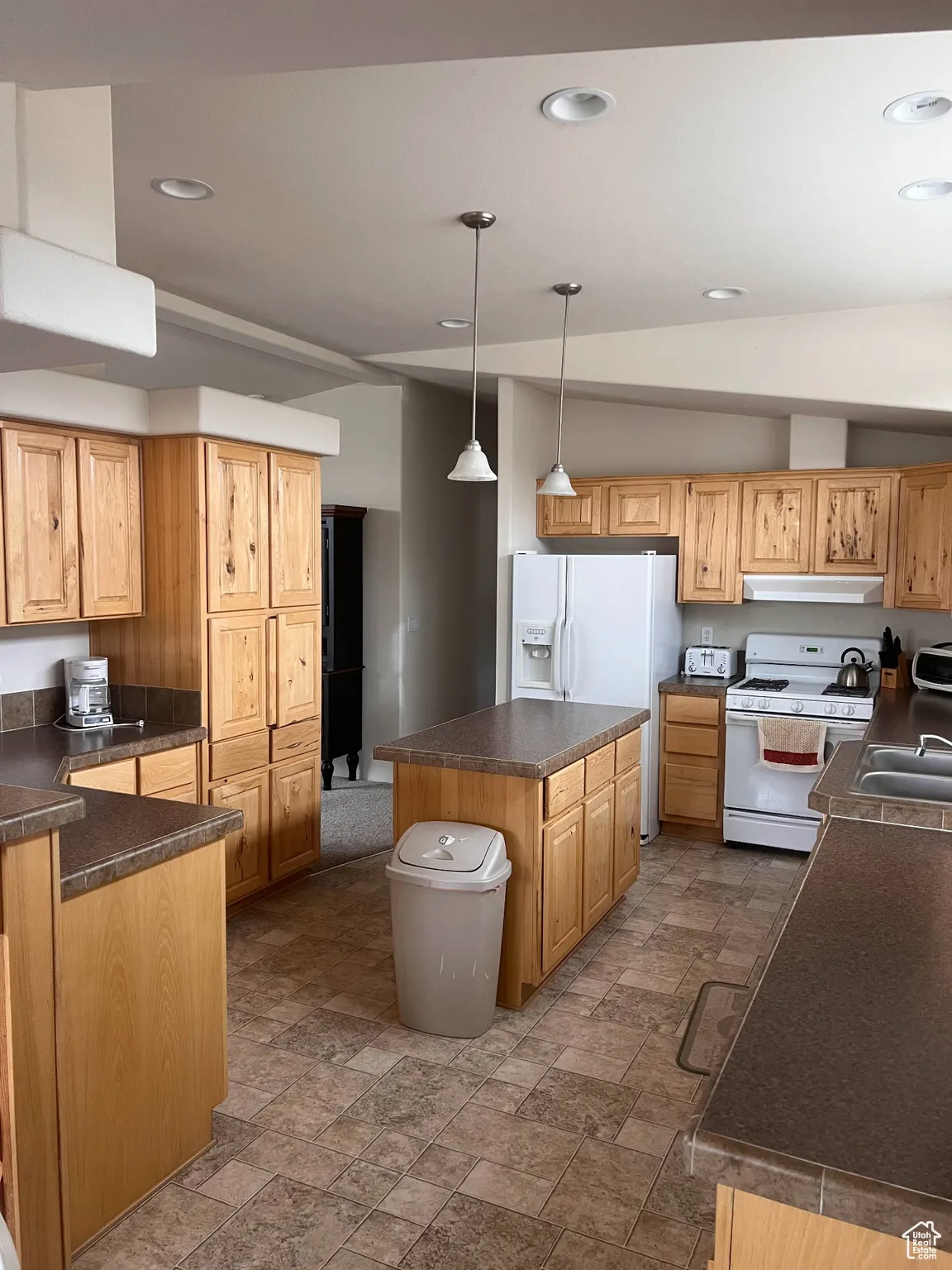 Kitchen with white appliances, under cabinet range hood, a kitchen island, dark countertops, and dark stone finish flooring