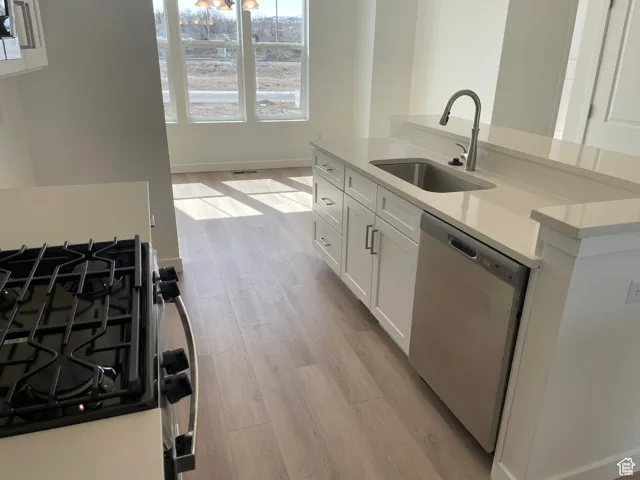 Kitchen with stainless steel dishwasher, light wood-style flooring, a sink, white cabinetry, and gas stove