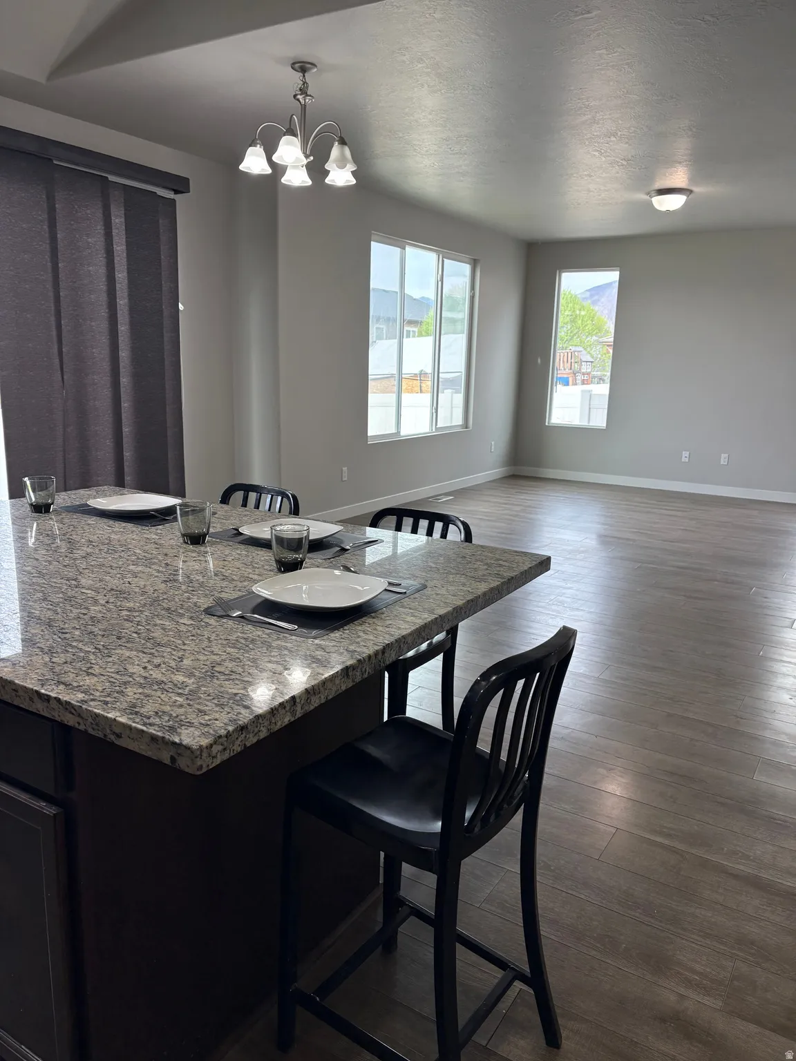 Kitchen with a breakfast bar area, dark wood-style floors, dark stone countertops, a textured ceiling, and suspended lighting