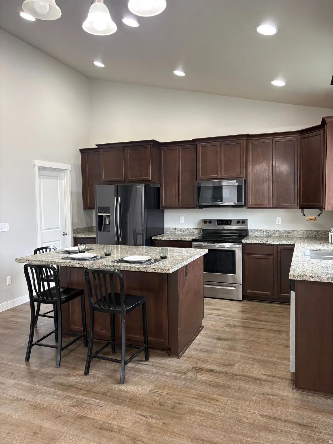 Kitchen featuring vaulted ceiling, stainless steel appliances, light stone counters, a center island, and dark wood finish cabinetry
