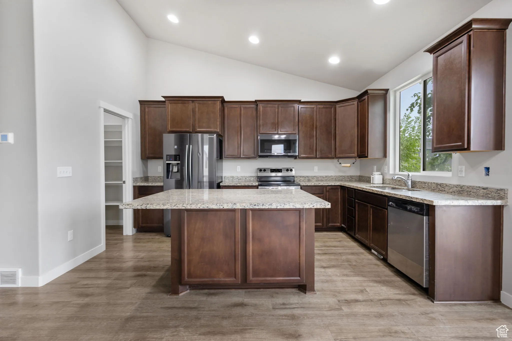 Kitchen with stainless steel appliances, a kitchen island, dark brown cabinetry, light wood finished floors, and recessed lighting