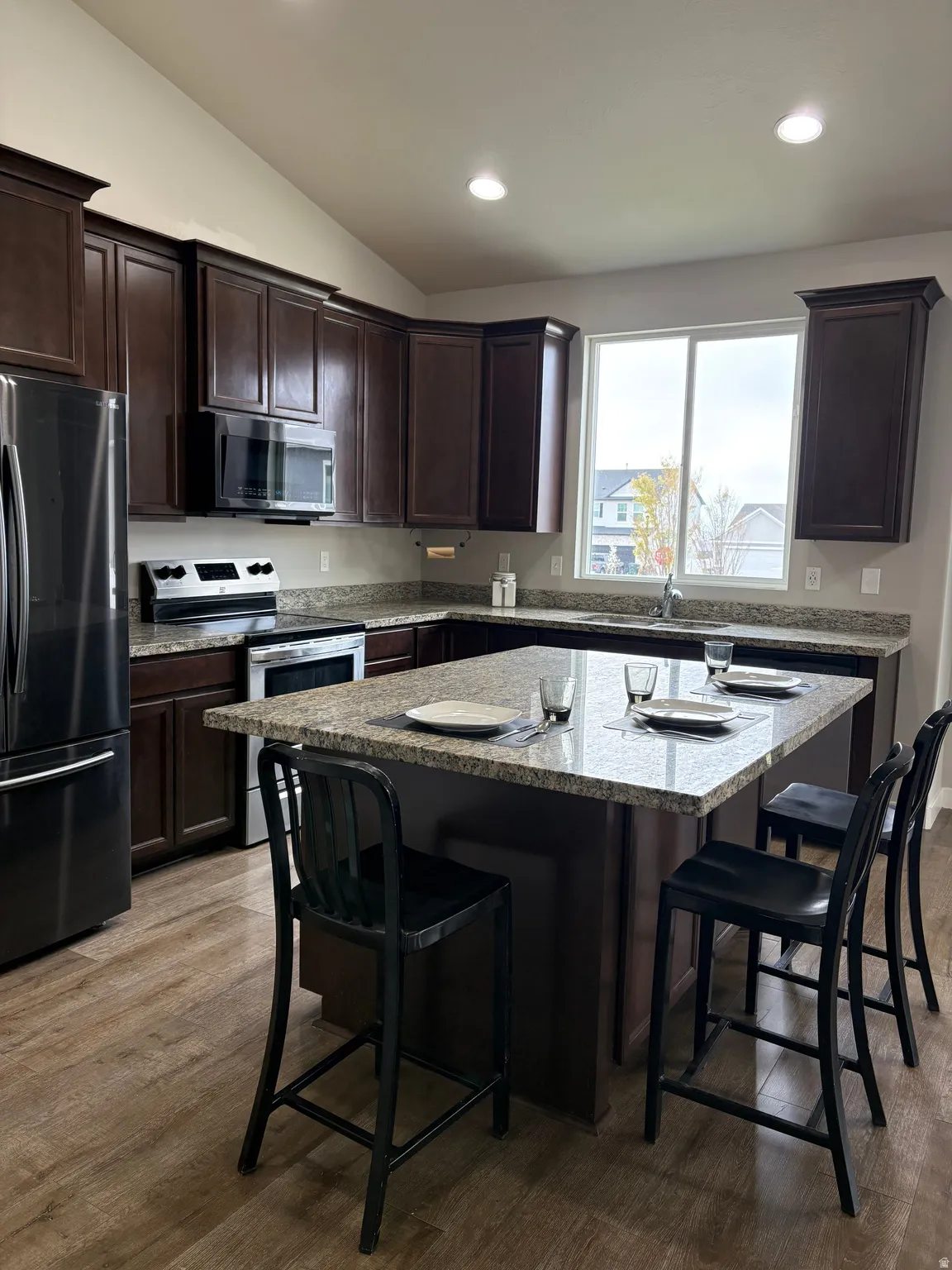 Kitchen featuring a breakfast bar, stainless steel appliances, dark wood finish cabinetry, vaulted ceiling, and recessed lighting