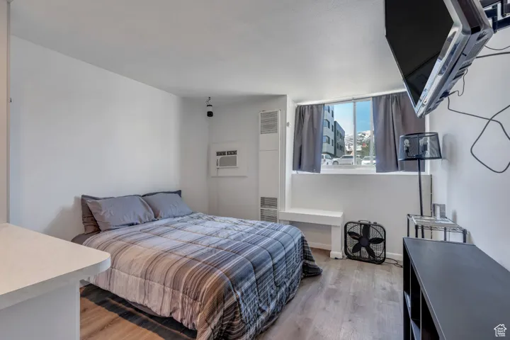 Bedroom with a wall mounted air conditioner, light wood finished floors, and baseboards