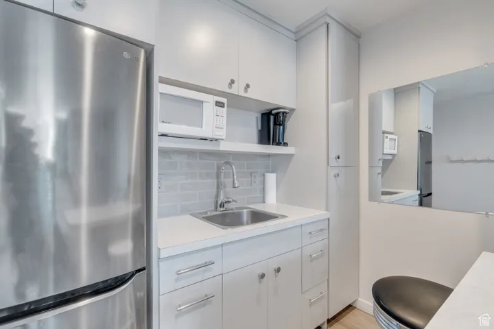 Kitchen featuring light countertops, a sink, white microwave, and freestanding refrigerator