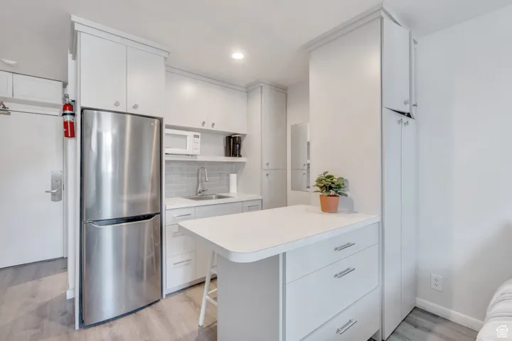 Kitchen with open shelves, a sink, freestanding refrigerator, light wood-type flooring, and white microwave