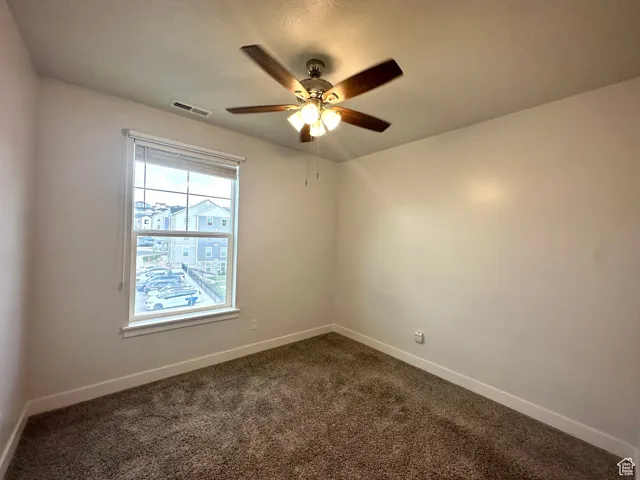 Empty room featuring a ceiling fan, visible vents, dark carpet, and baseboards
