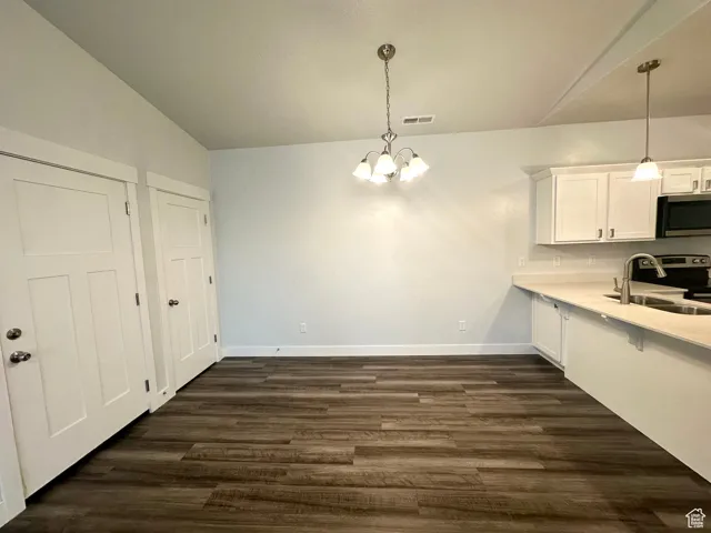 Kitchen featuring stainless steel appliances,  white cabinetry, a sink, and a notable chandelier