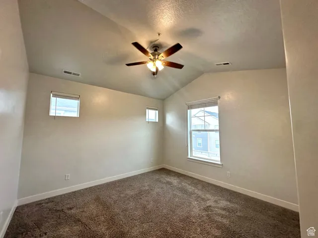 Unfurnished room with visible vents, ceiling fan, vaulted ceiling, and baseboards