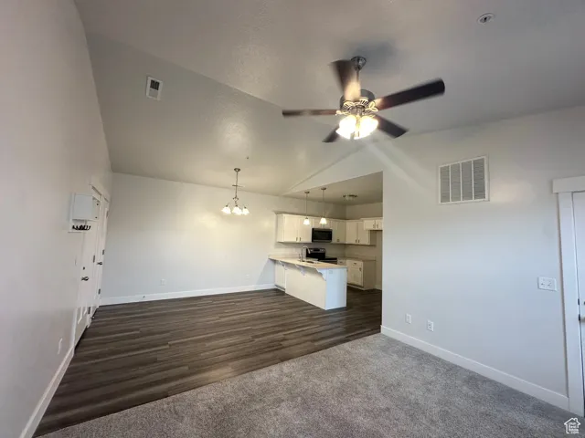 Unfurnished living room with dark wood-style flooring, ceiling fan with notable chandelier, baseboards