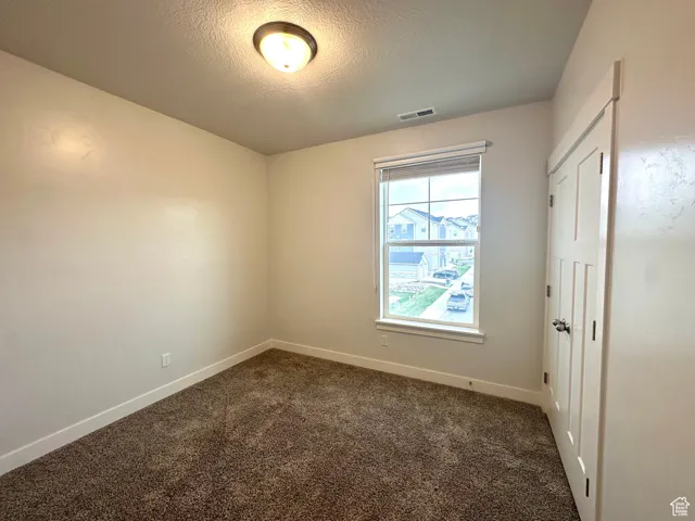 Empty room featuring a textured ceiling, visible vents, dark carpet, and baseboards